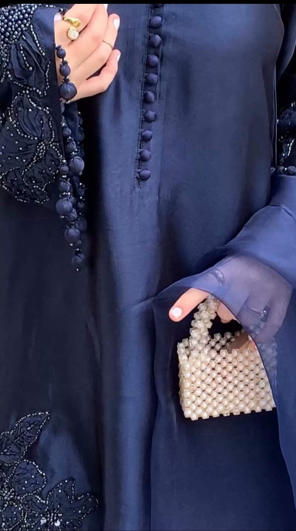 Person wearing a dark blue outfit with a beaded handbag