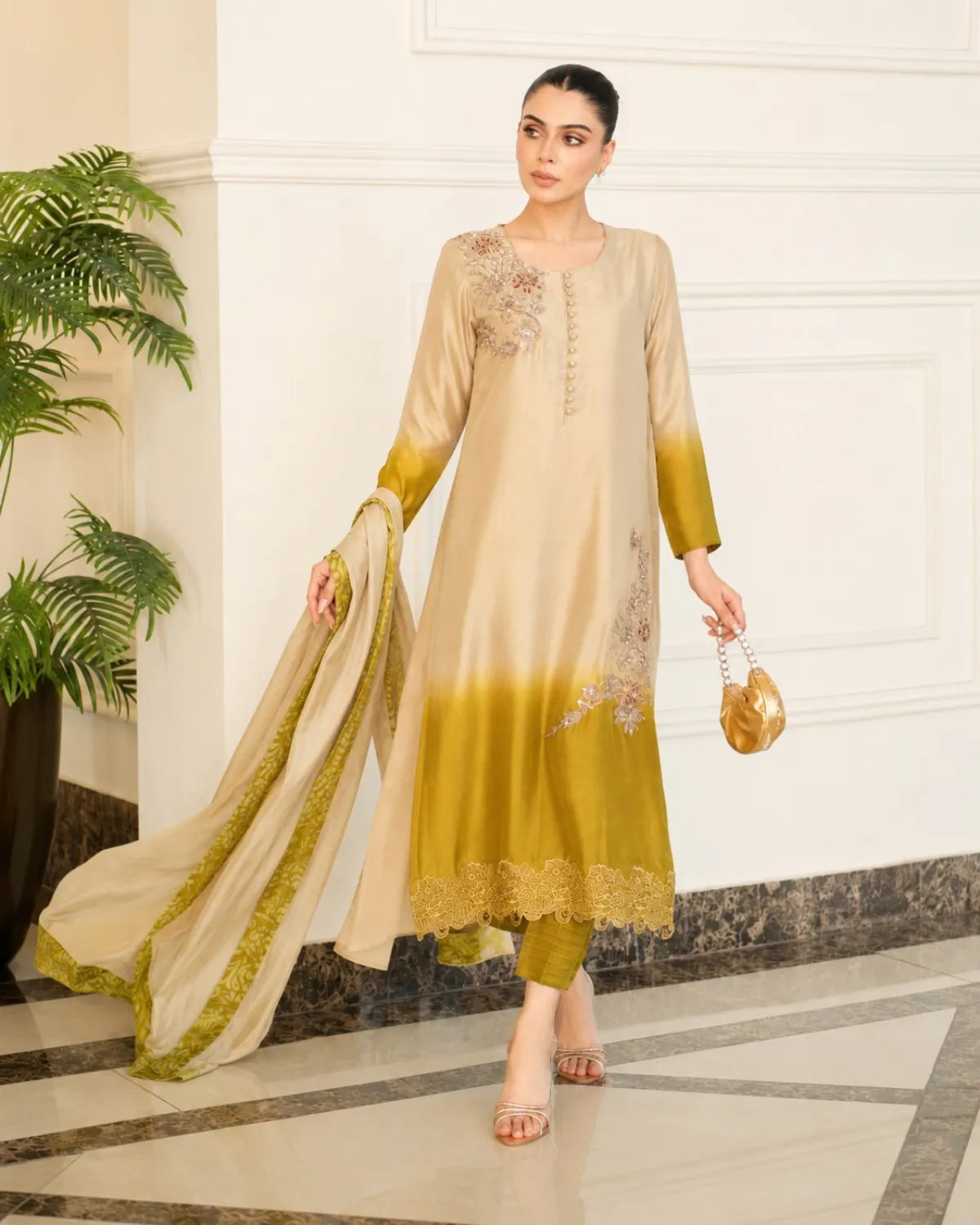 Woman in a beige and green traditional outfit standing in an elegant interior setting.