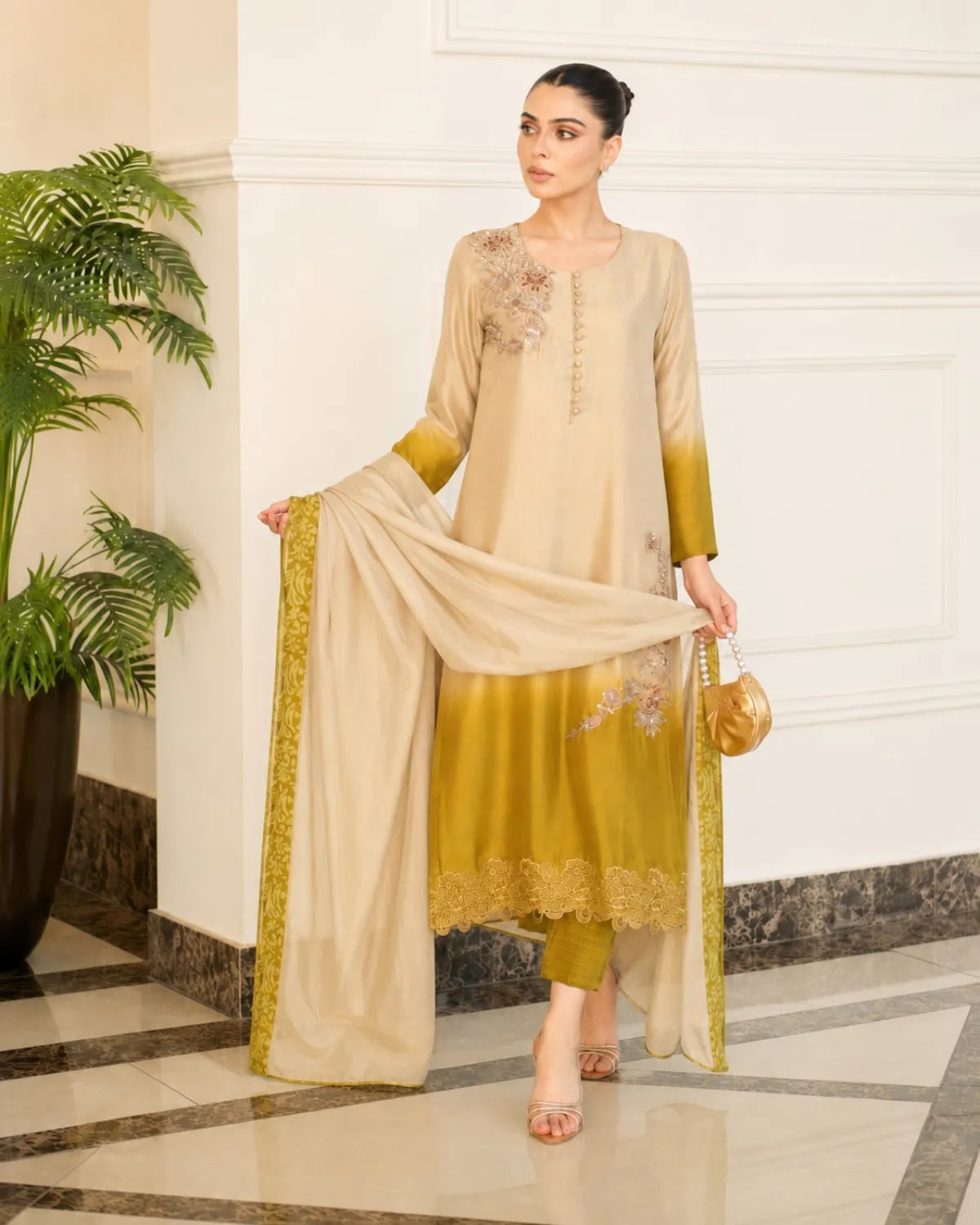 Woman in a beige and green traditional outfit with a matching dupatta, standing in an elegant interior setting.