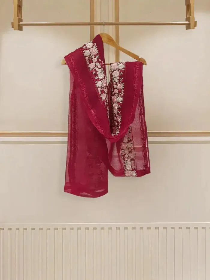 Red scarf with floral embroidery on a wooden hanger against a white wall.