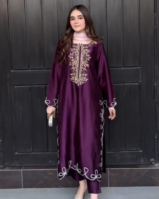 Woman wearing a purple dress with gold embroidery in front of a dark wooden door.