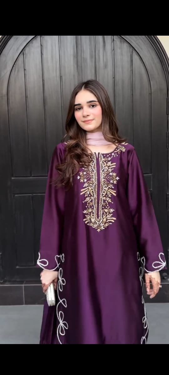 Woman wearing a purple dress with gold embroidery against a dark background