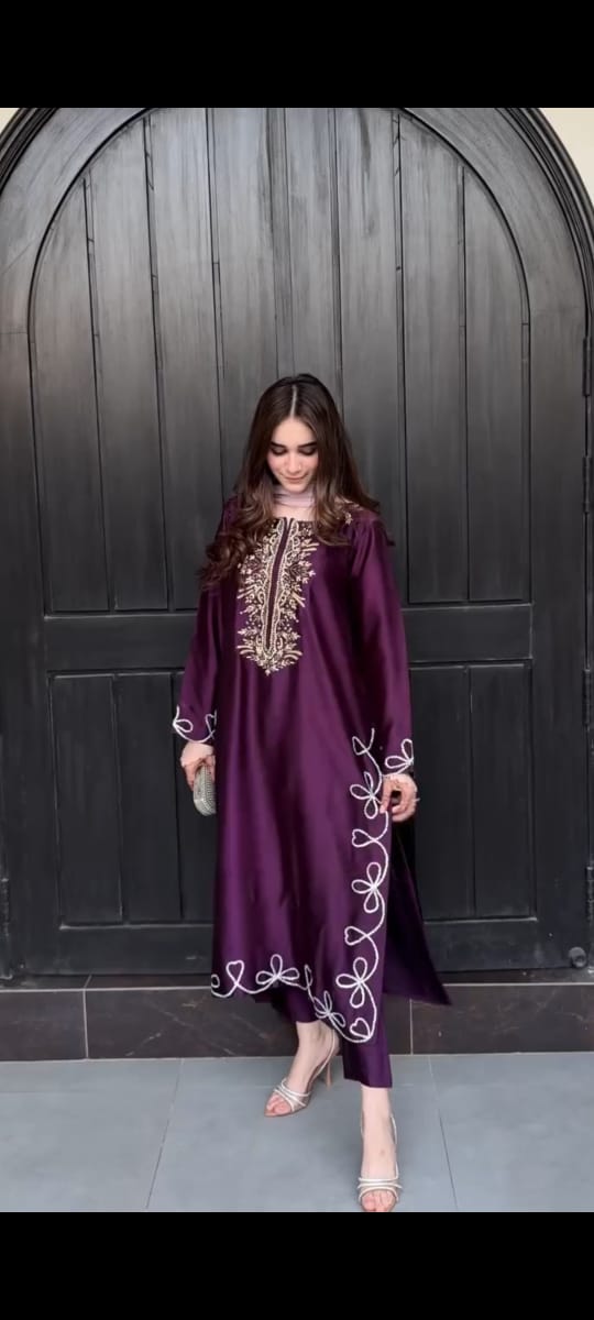 Woman wearing a purple embroidered dress standing in front of a dark wooden door.