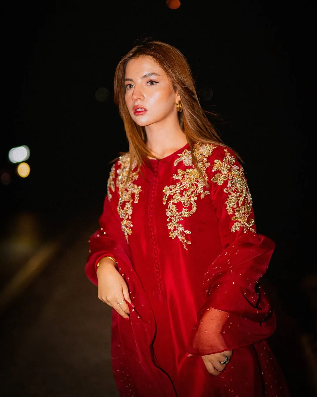 Woman wearing a red dress with gold embroidery at night.