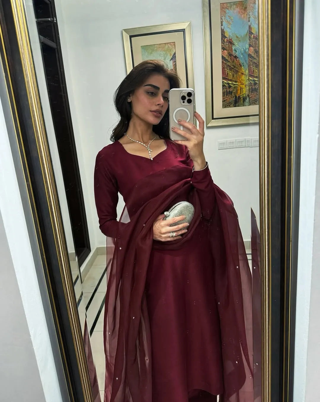 Woman taking a mirror selfie wearing a burgundy saree with a white background