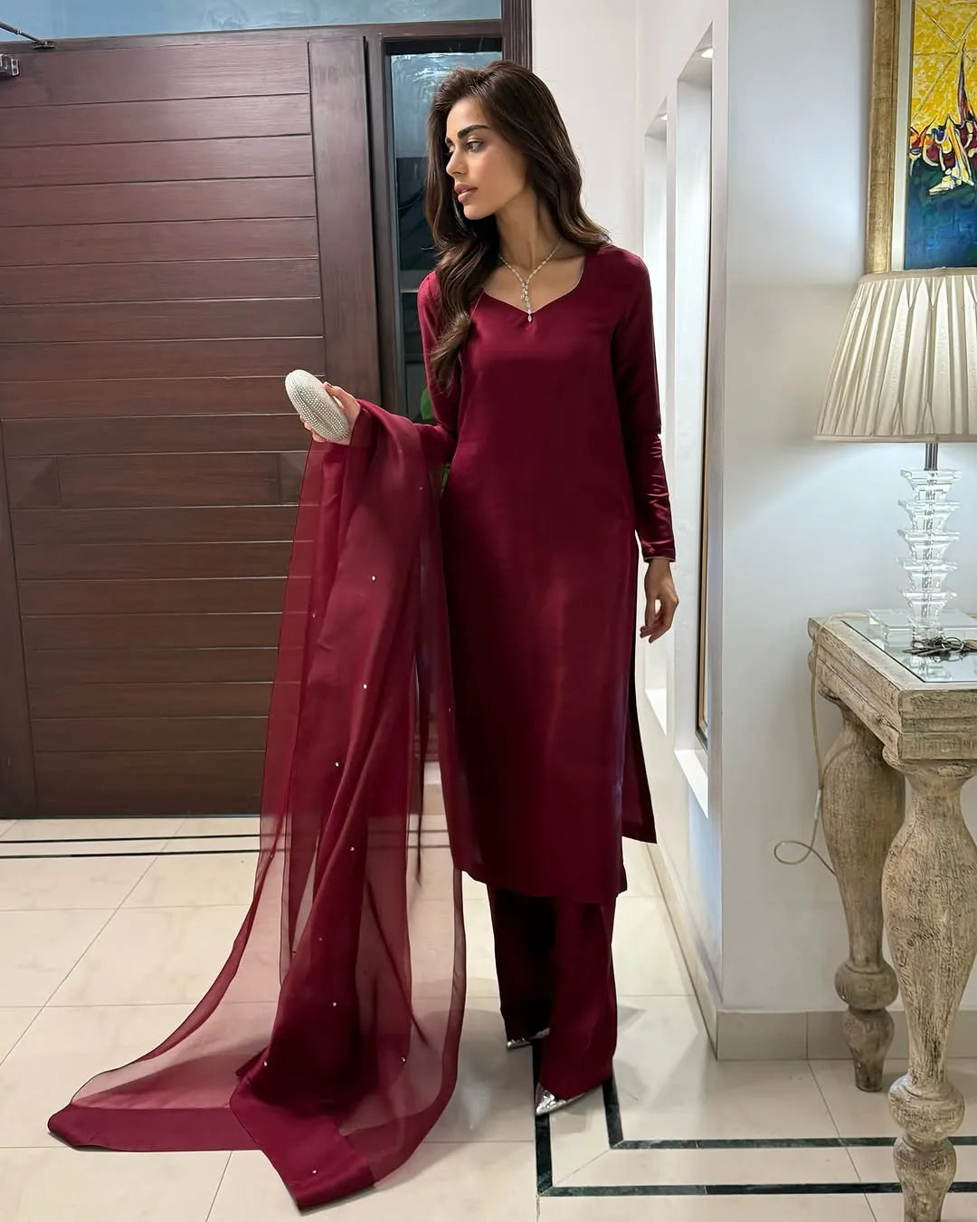 Woman in a maroon traditional outfit standing indoors.
