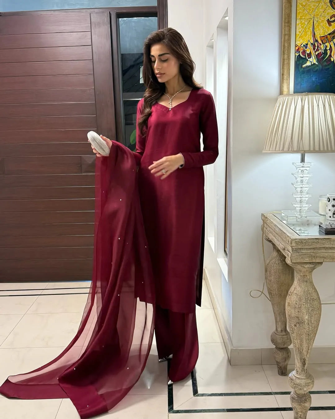 Woman in a burgundy traditional outfit holding a dupatta in a well-lit room.
