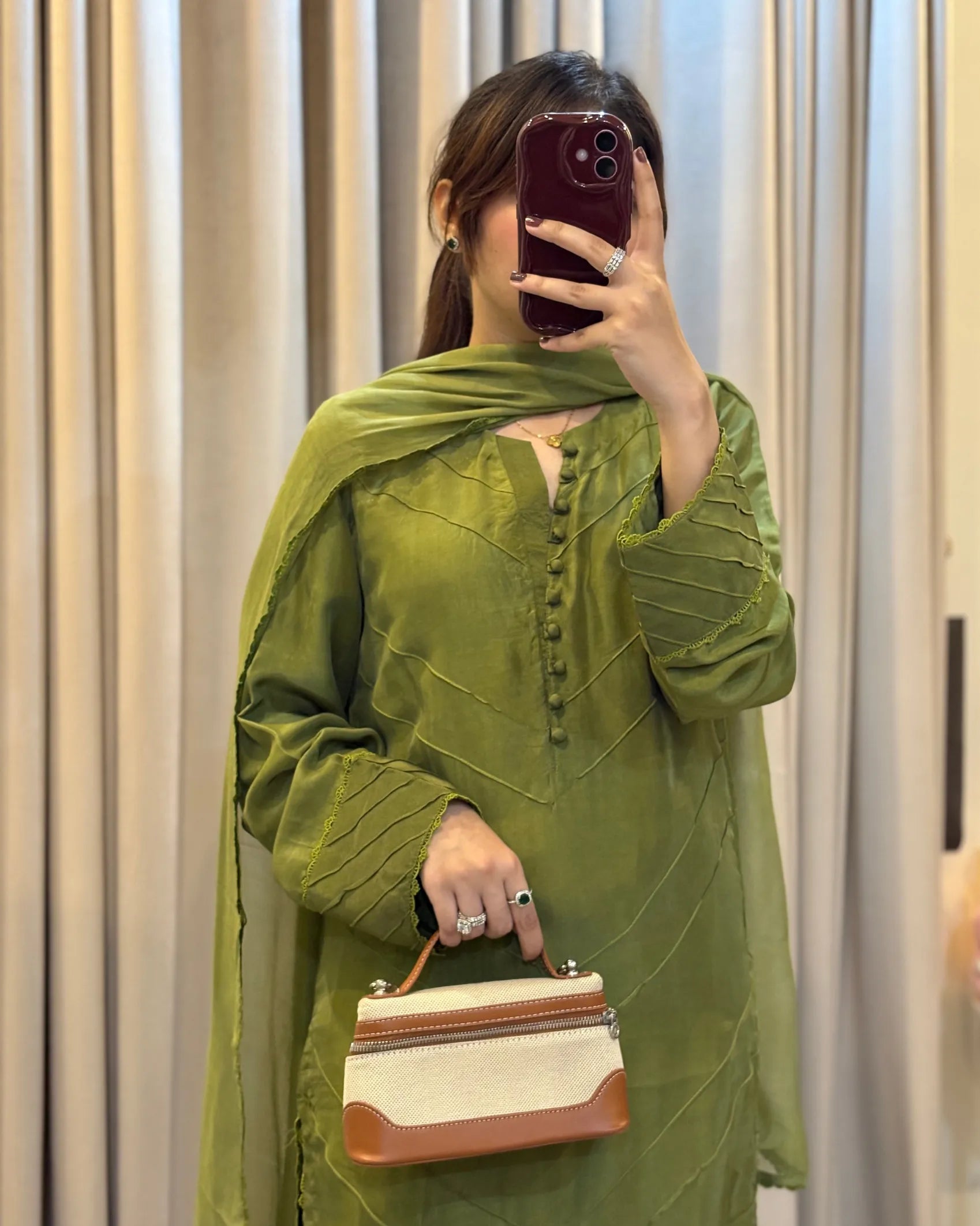 Person wearing a green outfit holding a handbag in front of a mirror.