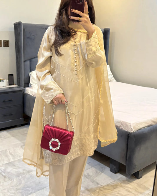 Person wearing a light yellow outfit with a red handbag in a bedroom setting