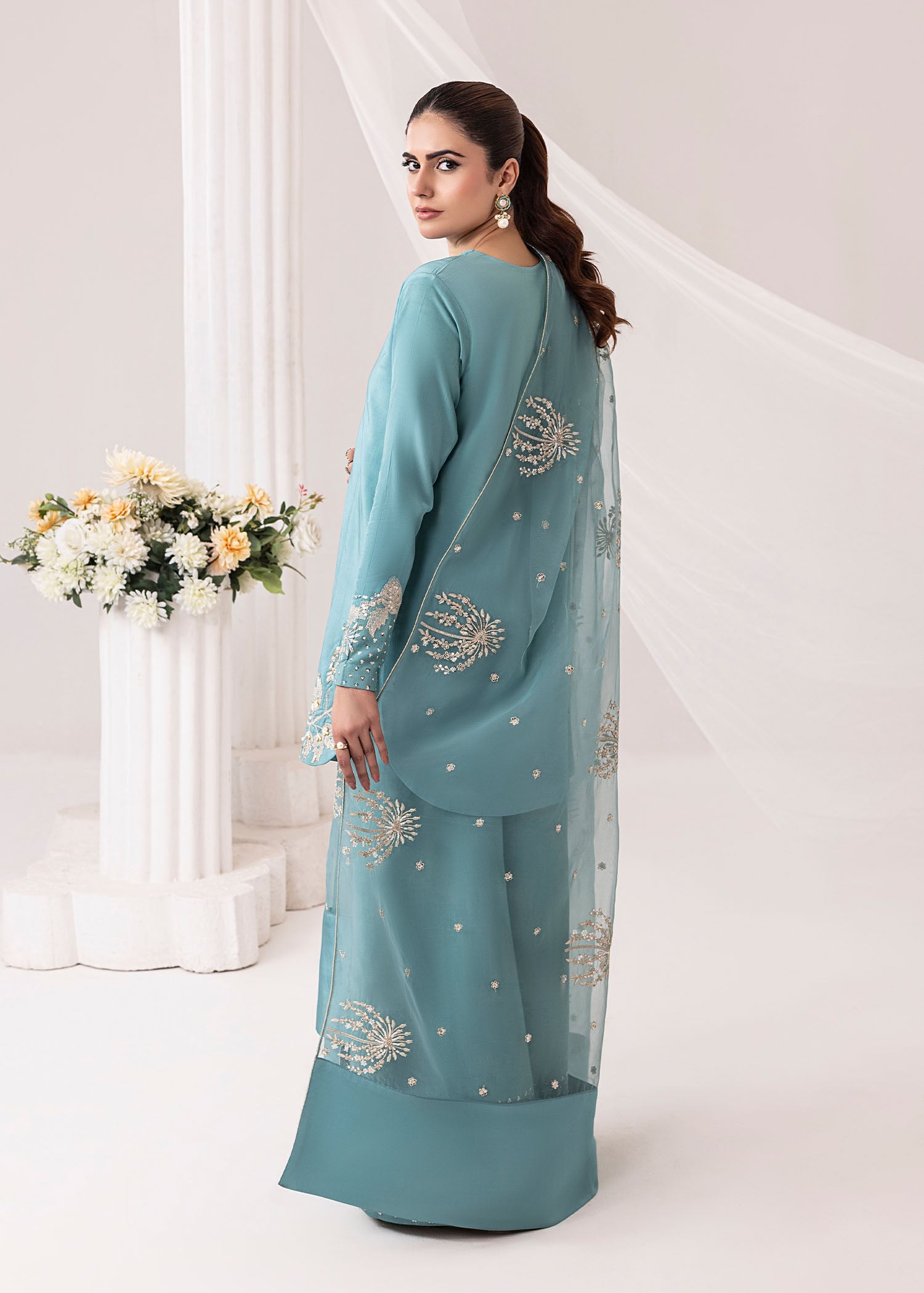 Woman wearing a teal embroidered outfit with a white background
