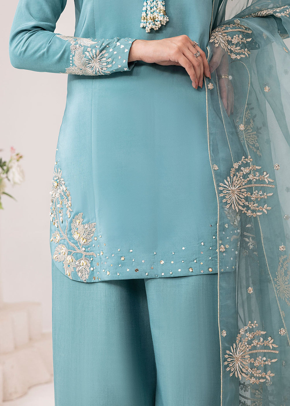 Teal traditional outfit with intricate gold embroidery on a light background