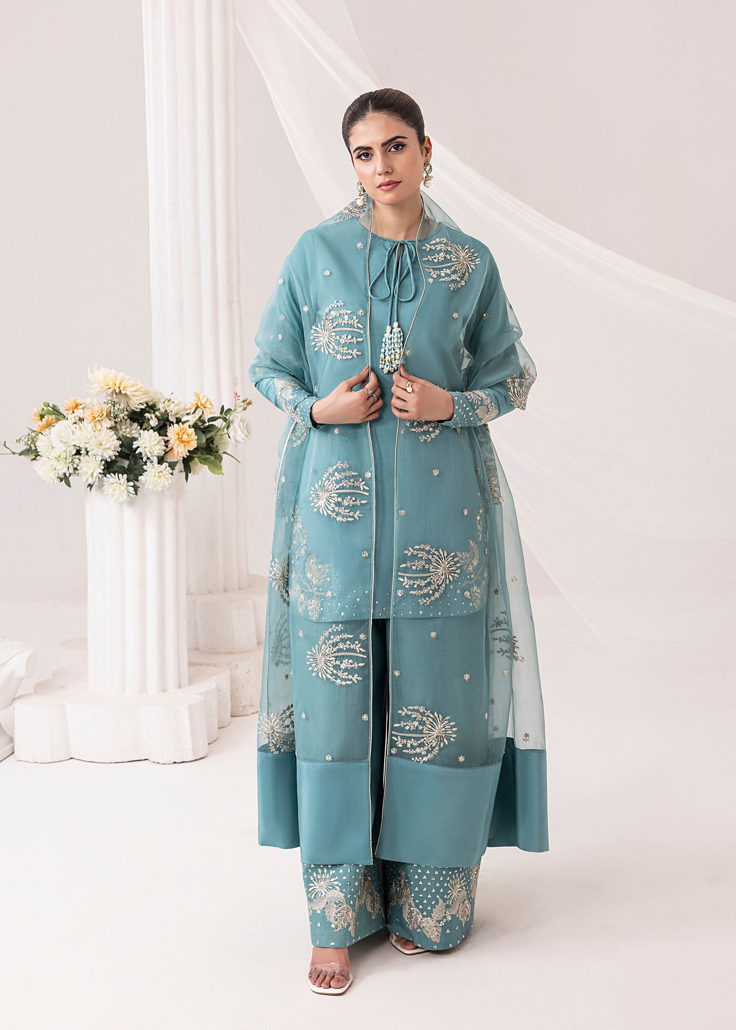 Woman wearing a light blue embroidered traditional outfit with a white background