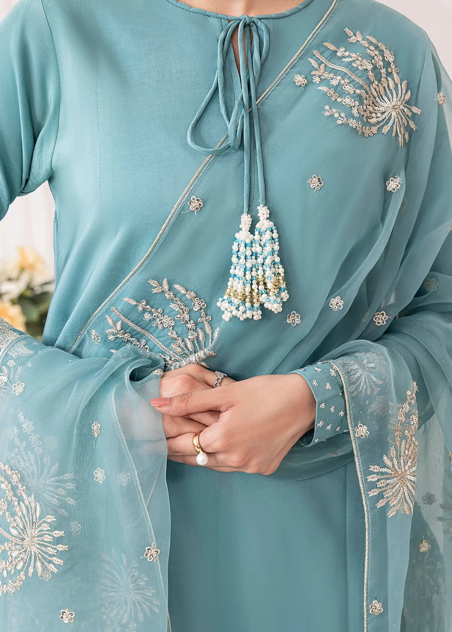 Teal embroidered outfit with intricate designs and tassels.