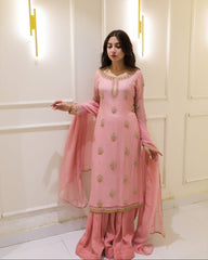 Woman in a pink traditional outfit standing against a white wall with decorative lights.
