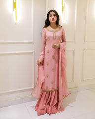 Woman in a pink traditional outfit standing against a white wall with decorative lights.