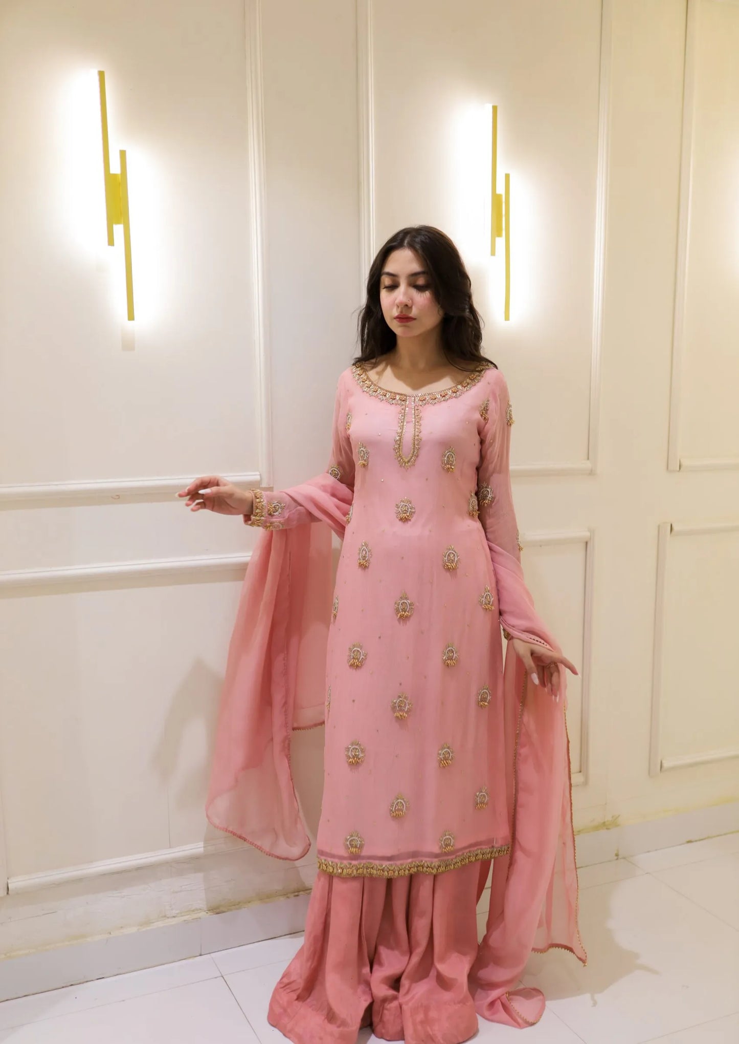 Woman in a pink traditional outfit standing against a white wall.