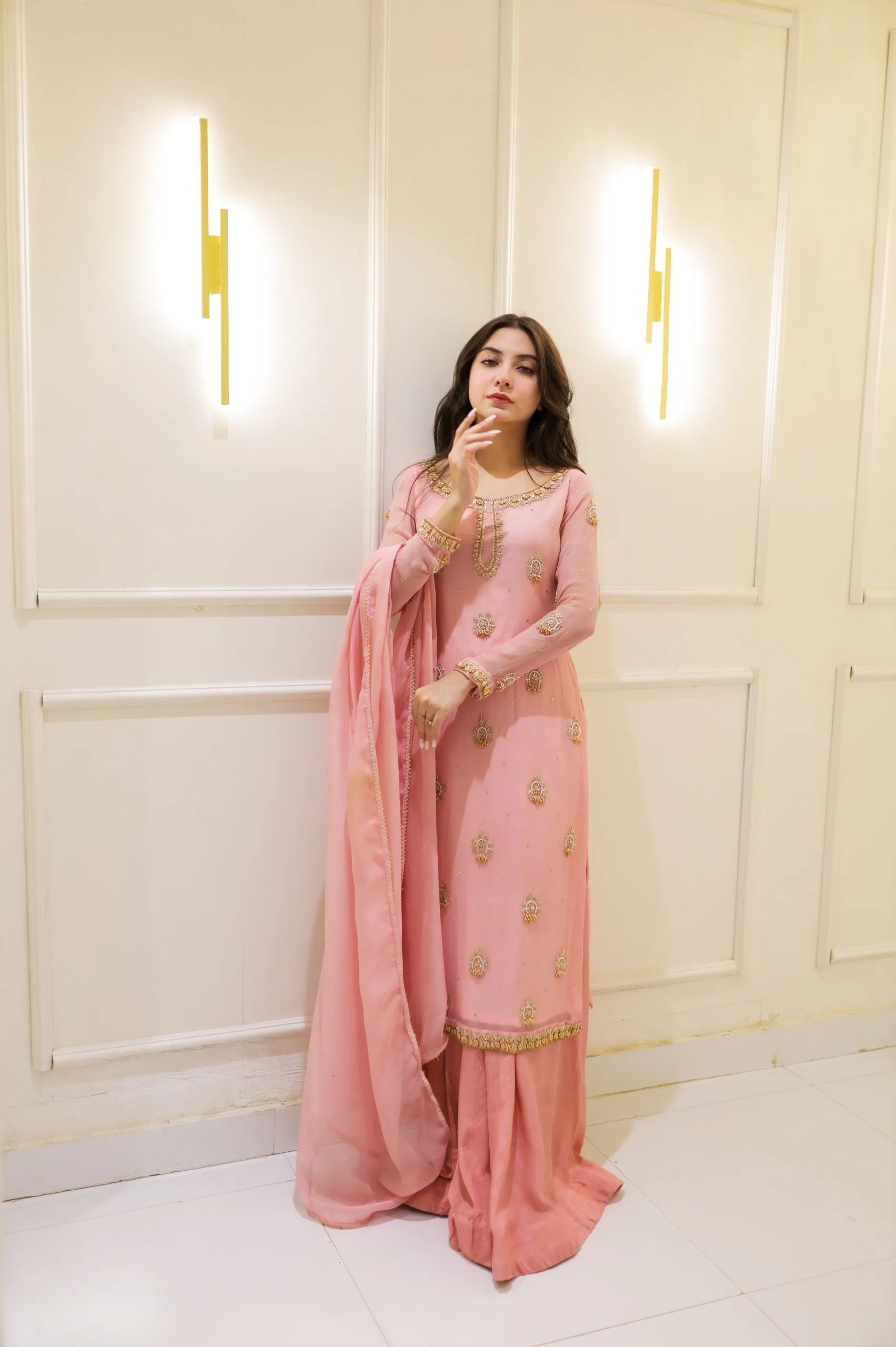 Woman in a pink traditional outfit standing against a white paneled wall.