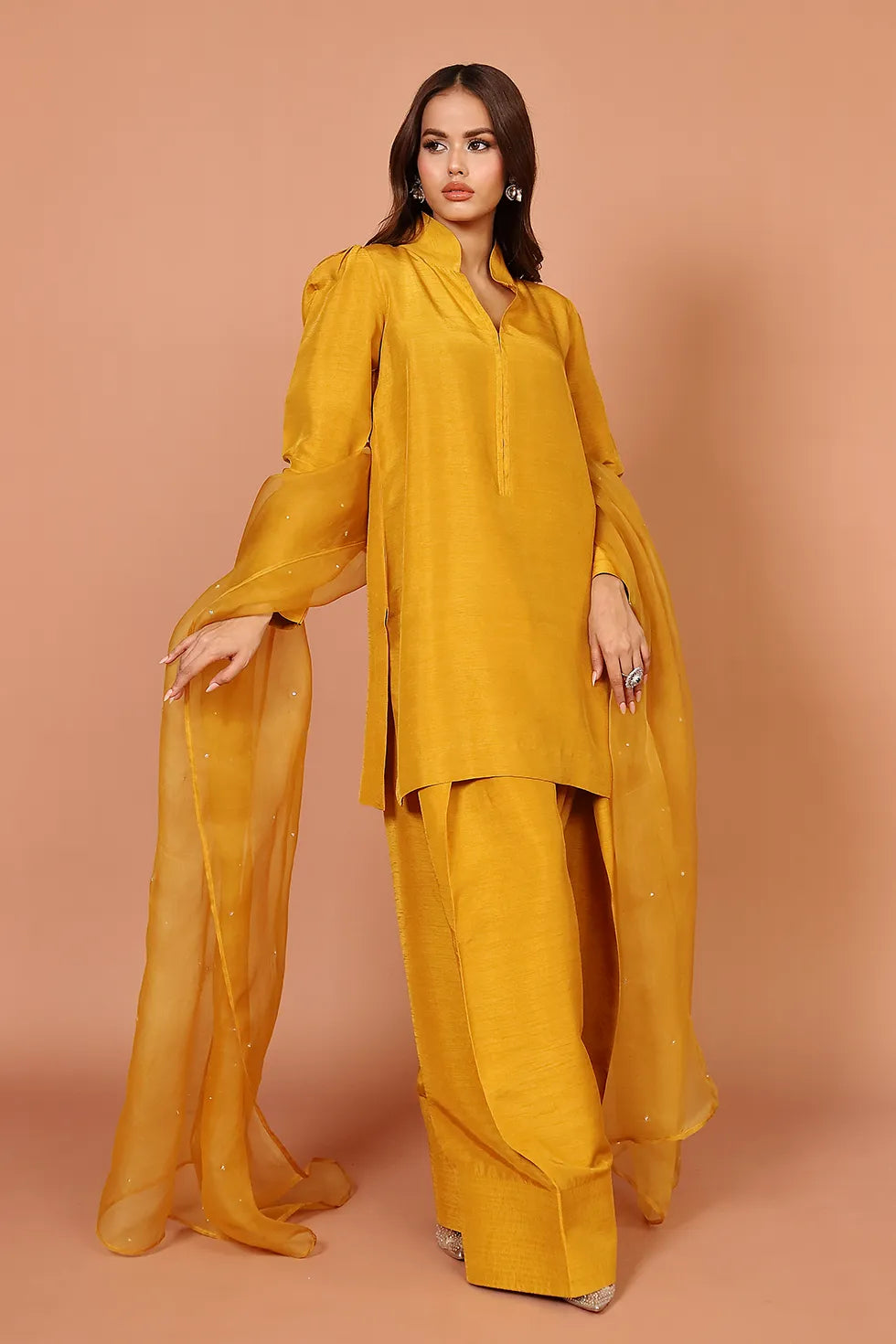 Woman wearing a mustard yellow outfit against a beige background