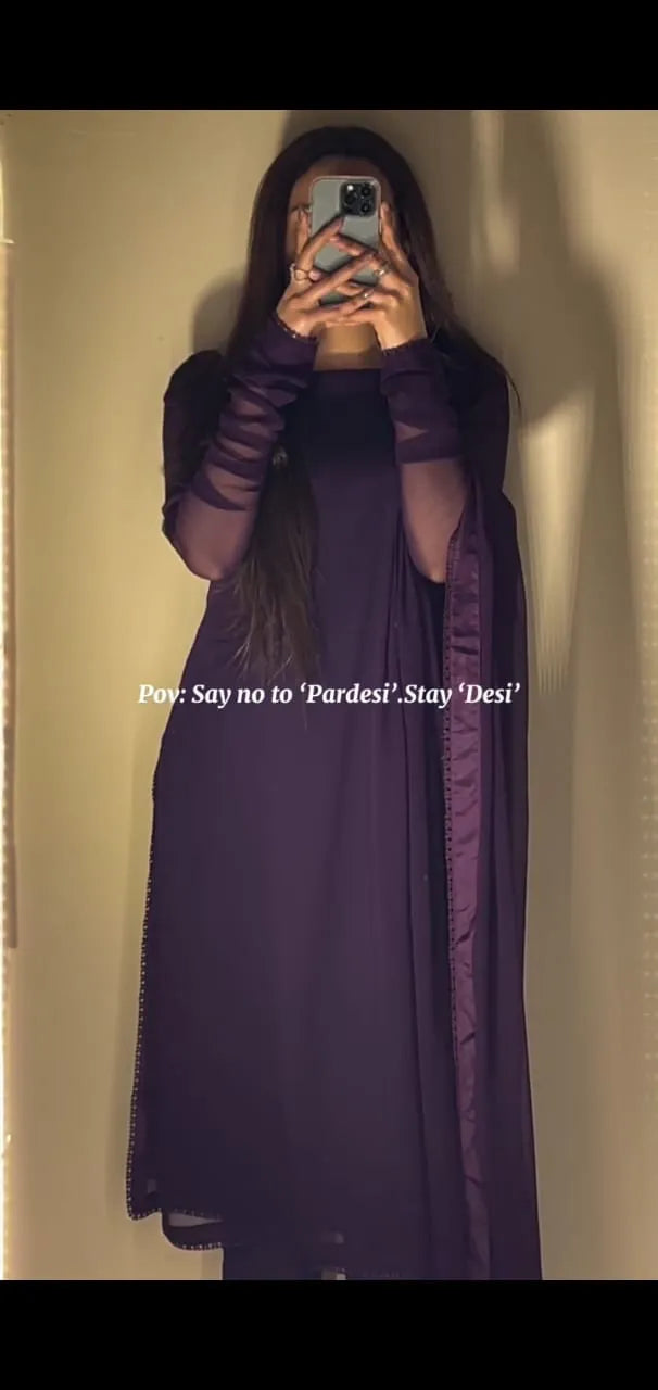 Person wearing a long purple dress with sheer sleeves against a plain background.