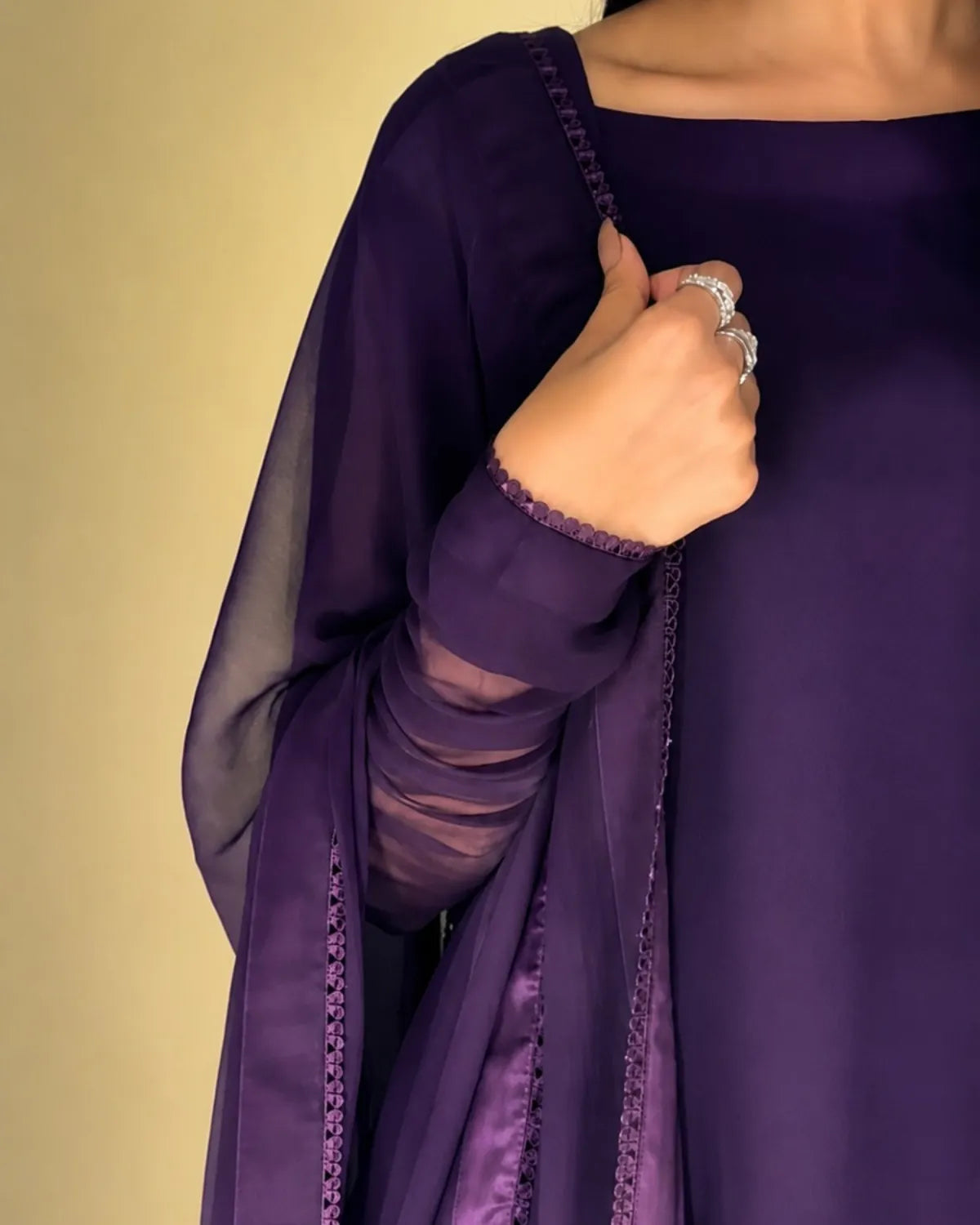 Close-up of a person wearing a purple garment with sheer sleeves against a beige background