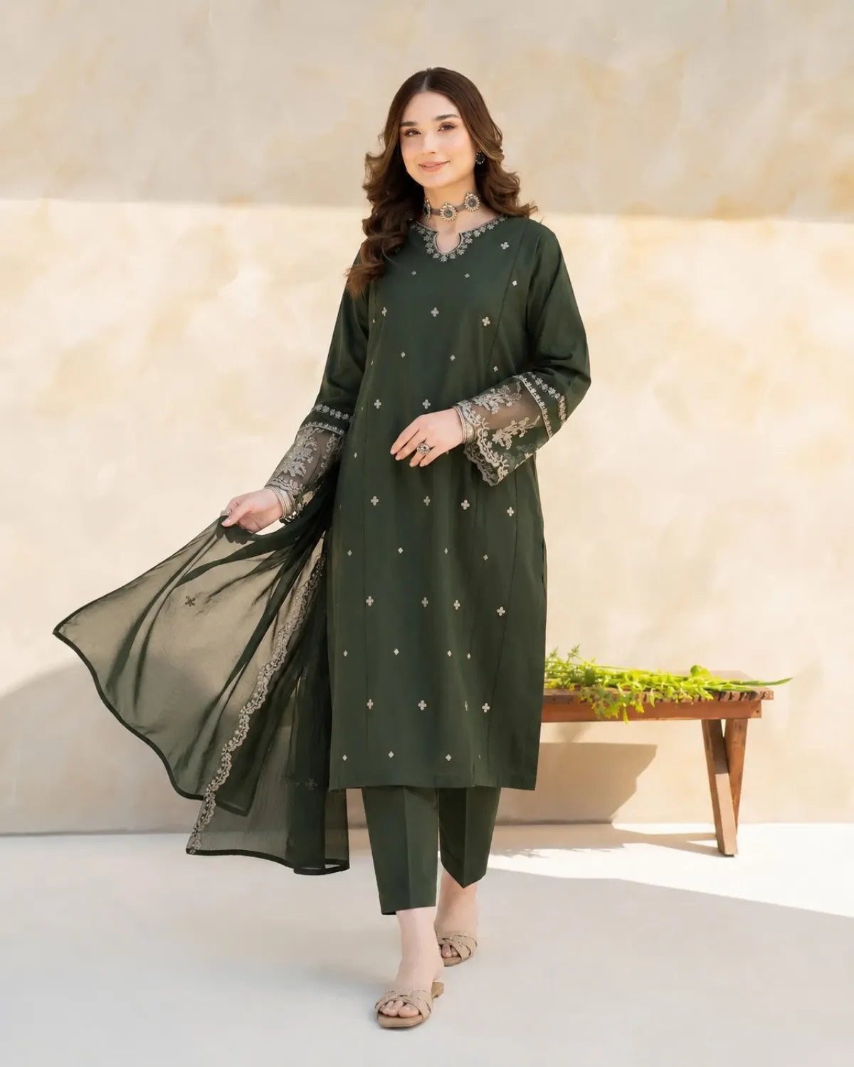 Woman wearing a green traditional outfit with embroidery in a minimalistic setting.