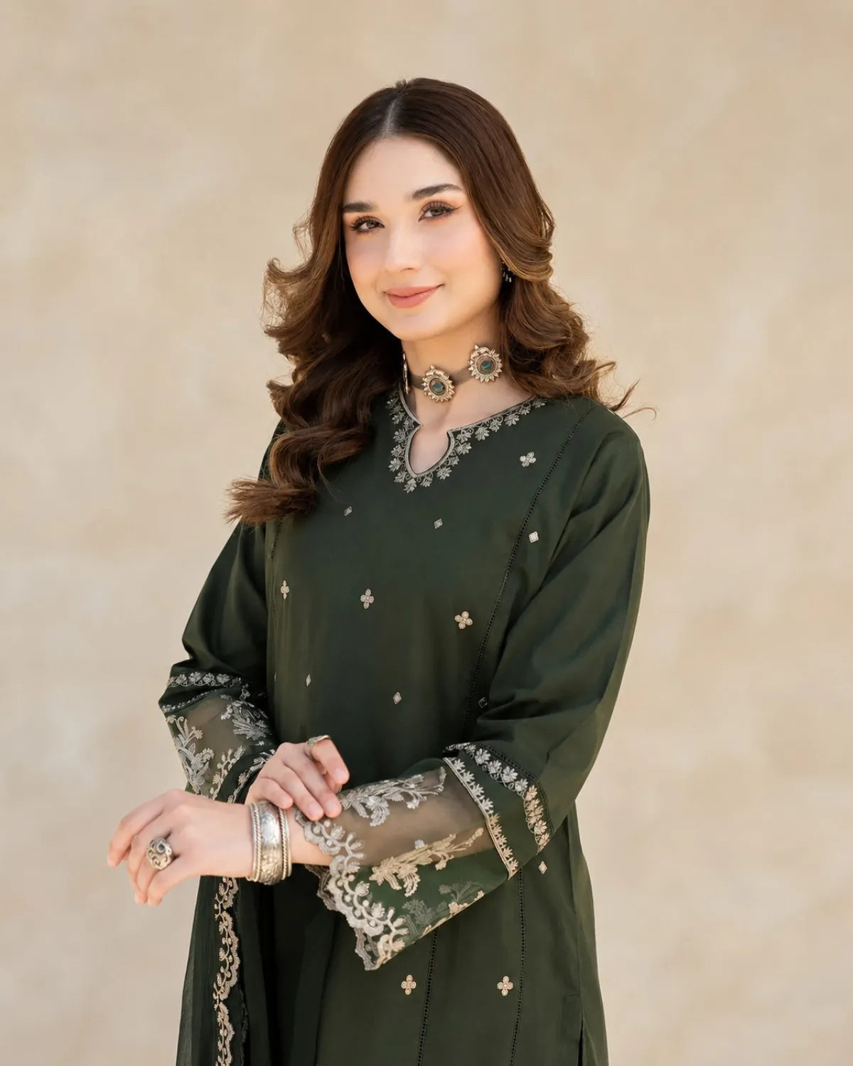 Woman wearing a dark green traditional outfit with intricate designs on a beige background