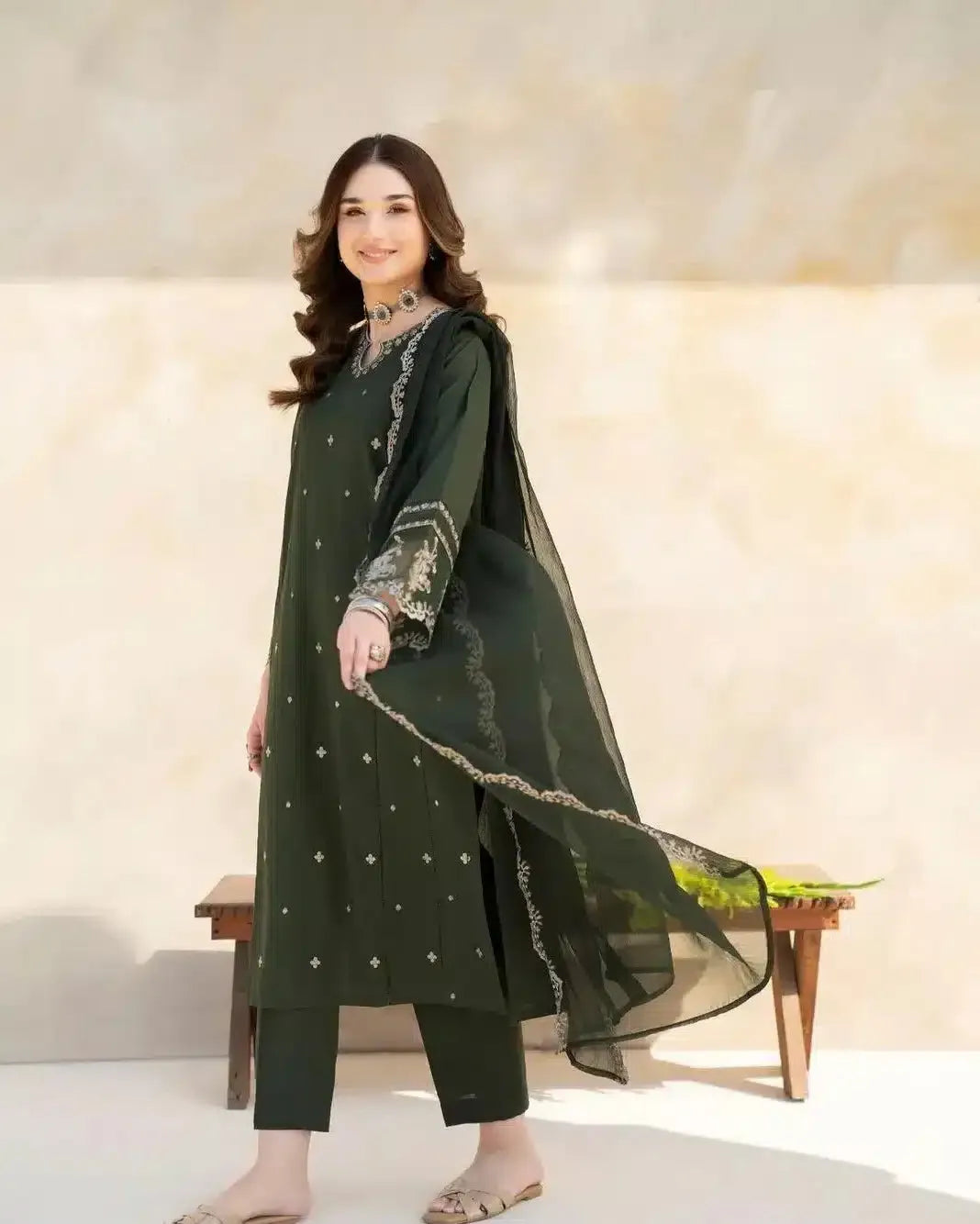 Woman wearing a green traditional outfit with a sheer dupatta against a neutral background