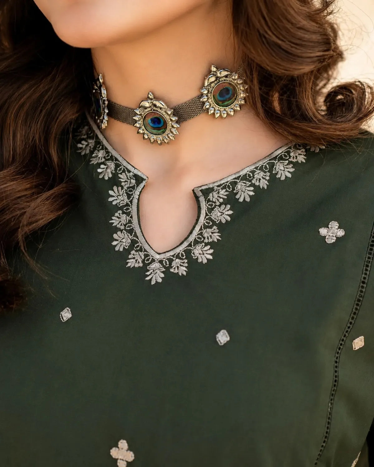 Close-up of a person wearing a green outfit with intricate silver embroidery and jewelry.