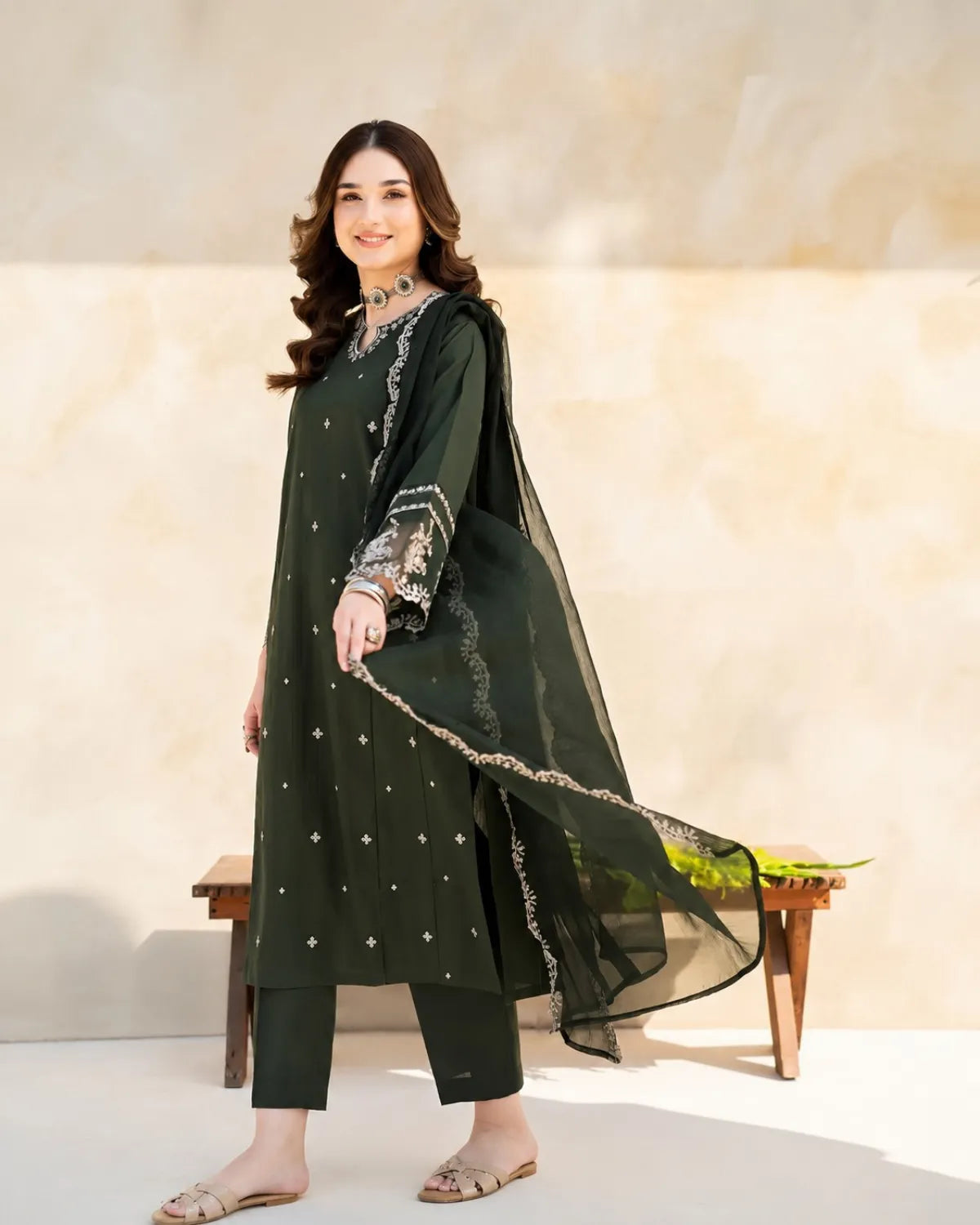 Woman wearing a green traditional outfit with a sheer dupatta against a beige background