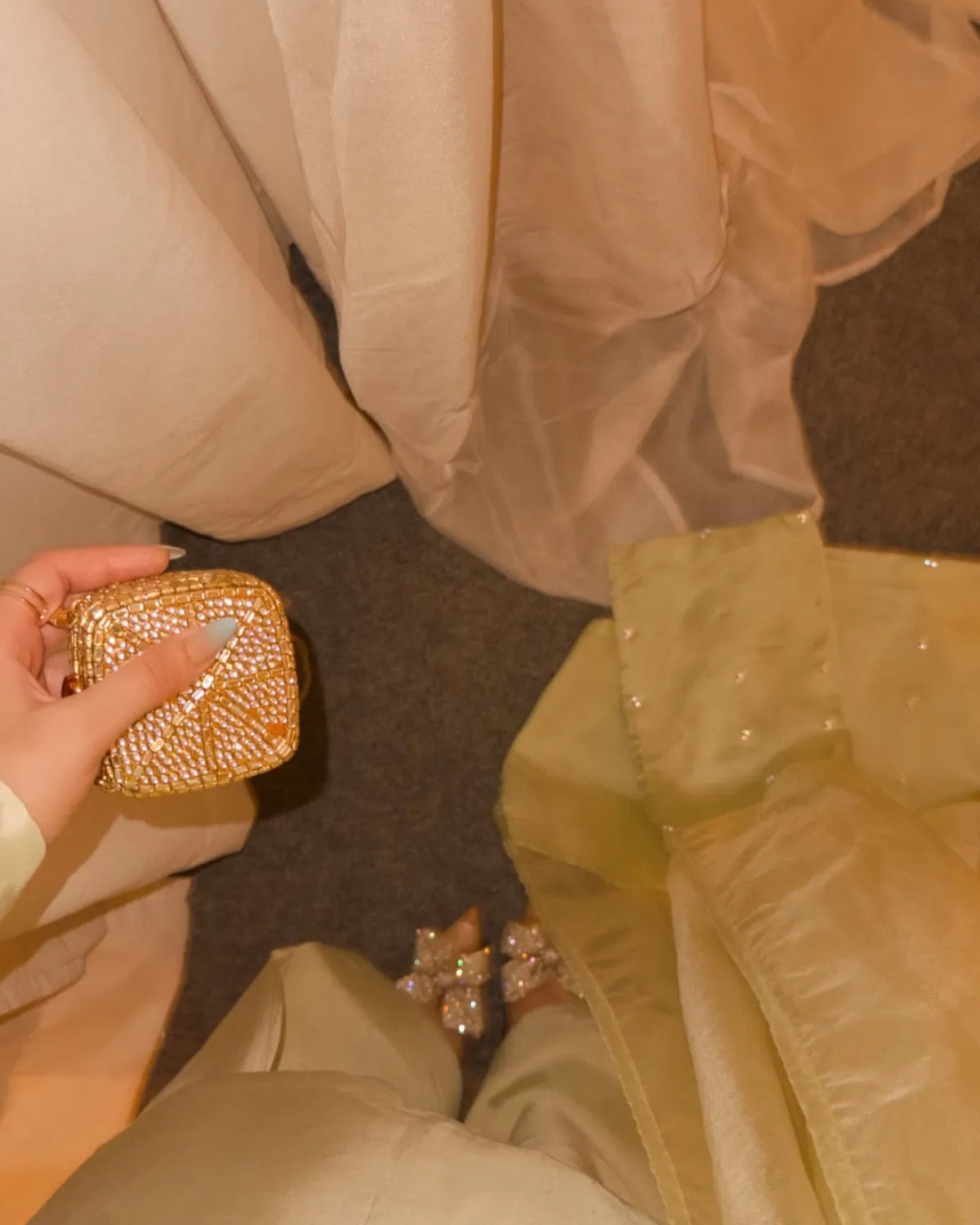 Person holding a gold clutch with matching shoes in a beige outfit.