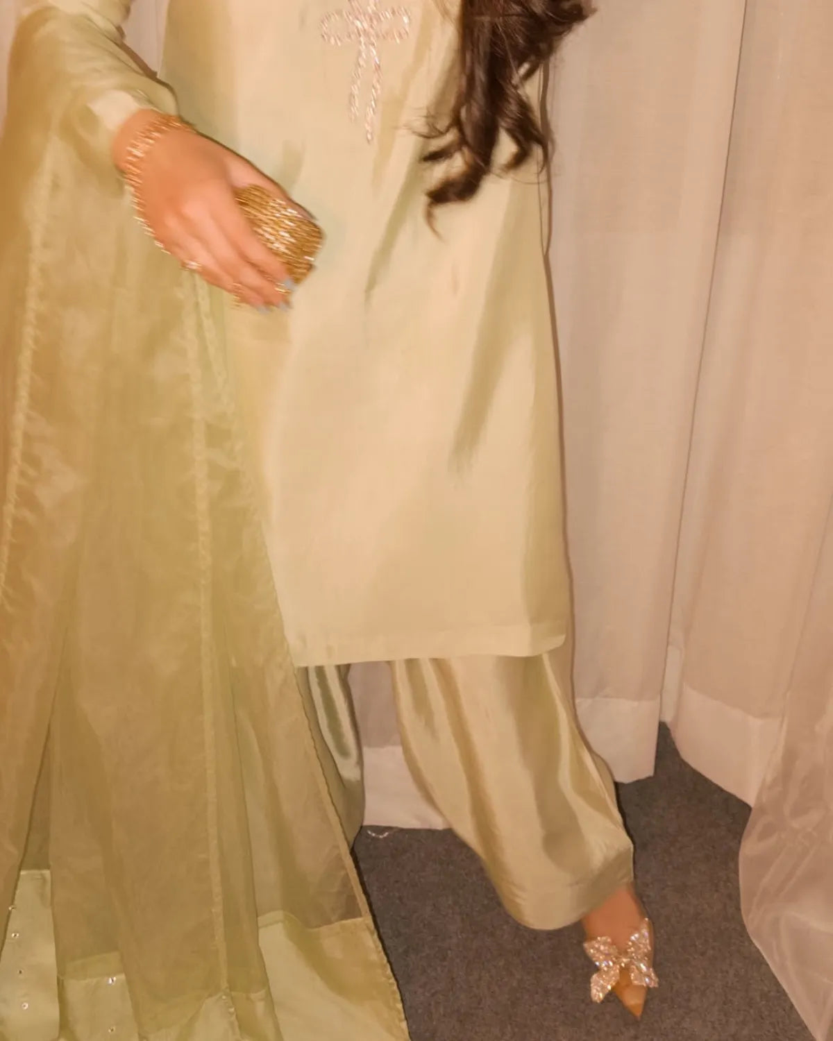 Light green traditional outfit with gold jewelry on a neutral background
