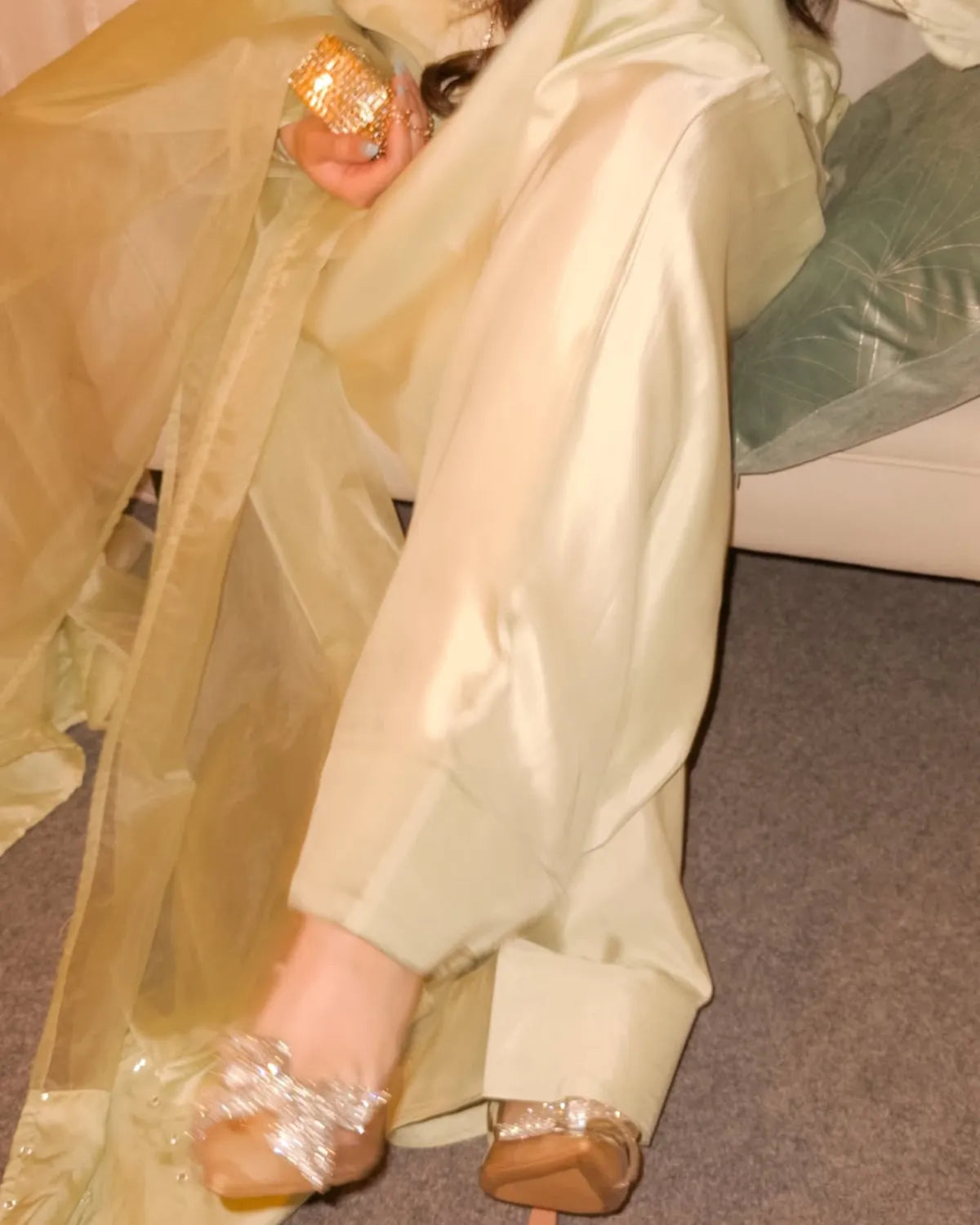 Person wearing a beige outfit with sheer overlay sitting on a couch.