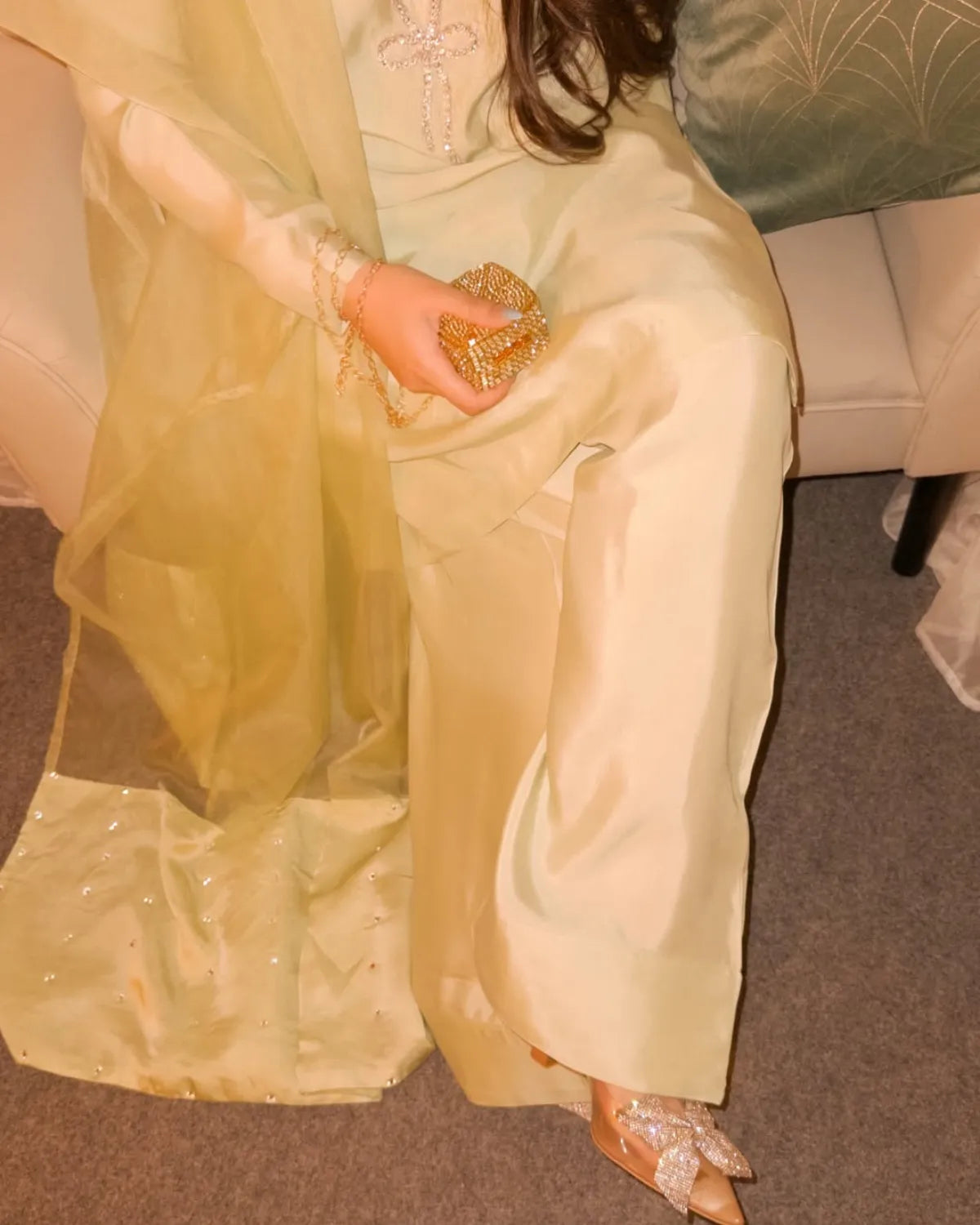 Person wearing a light green traditional outfit with a gold clutch and shoes.