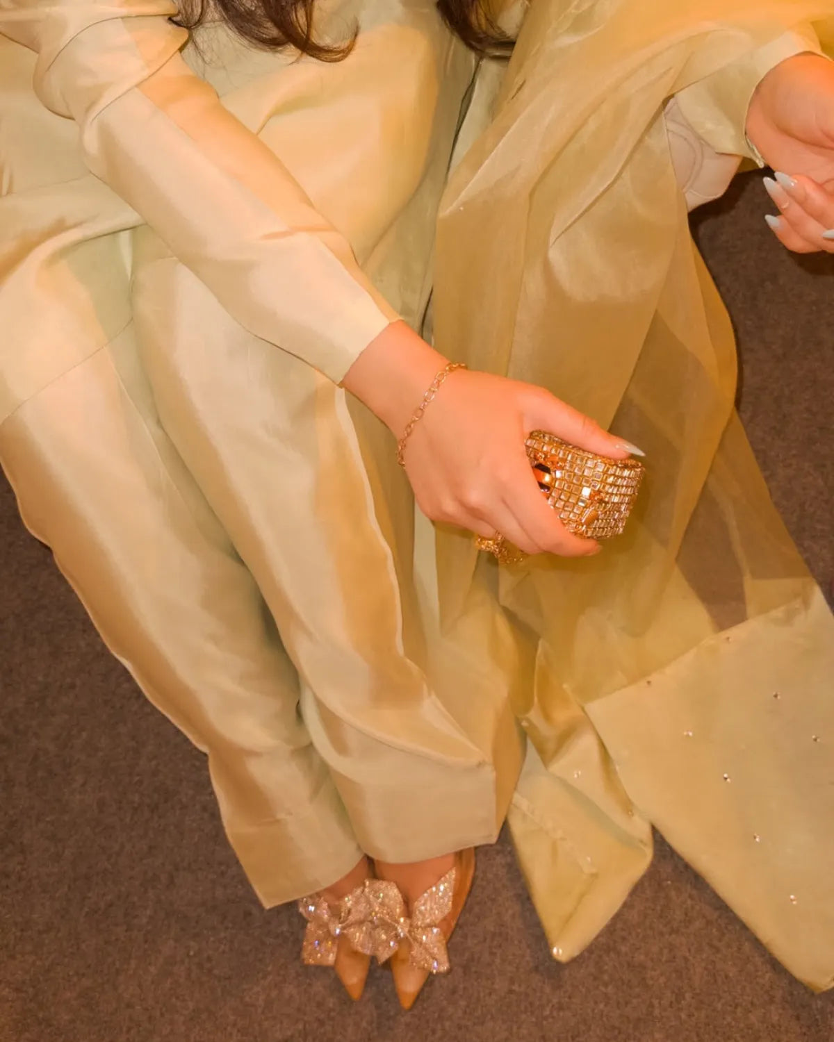 Person wearing a light green outfit with gold jewelry on a brown floor.