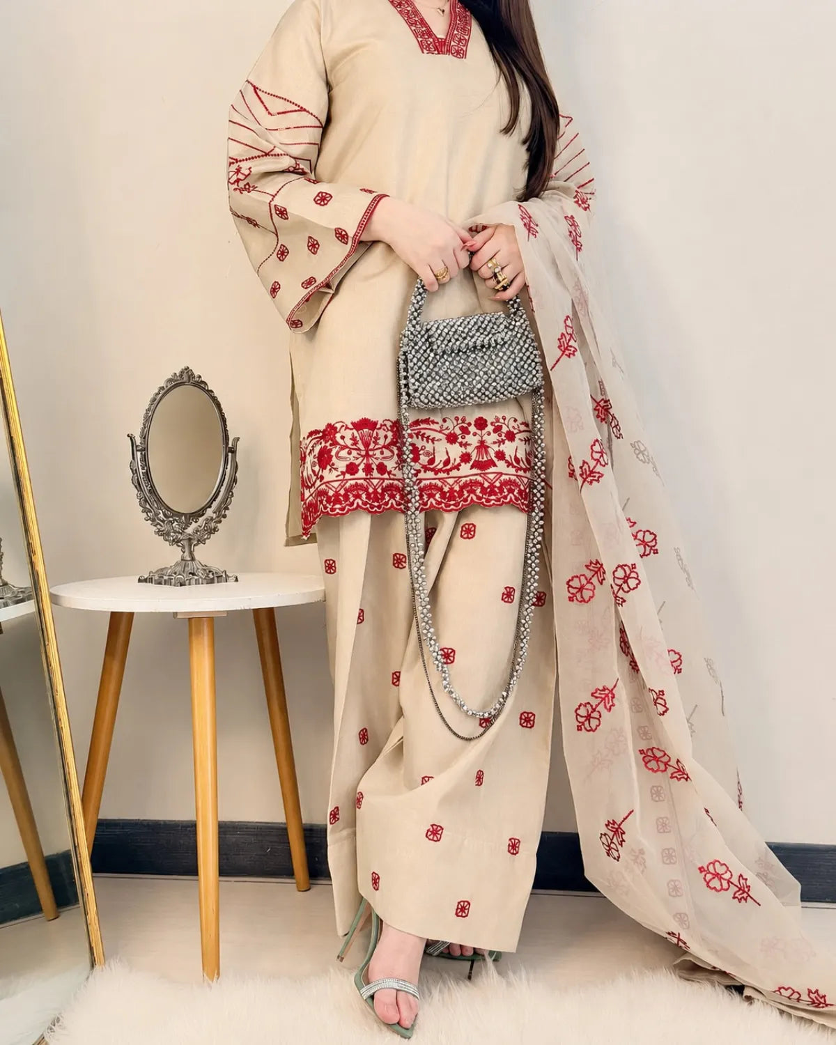 Woman wearing a traditional outfit with red embroidery in a minimalistic room.