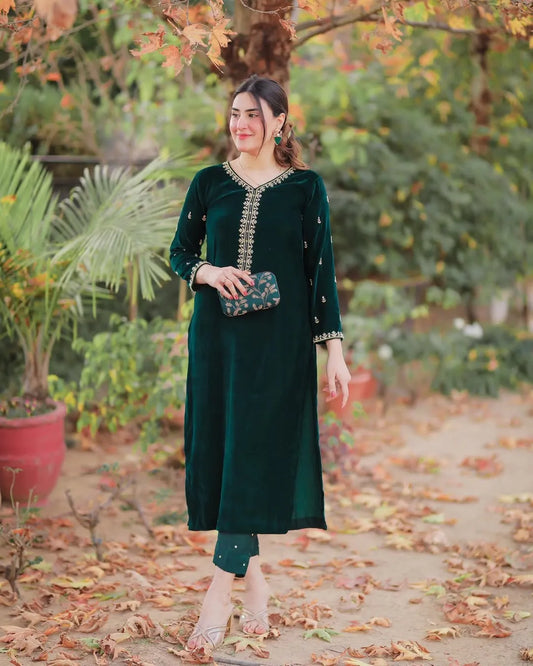 Woman in a green traditional outfit standing in a garden with autumn leaves.