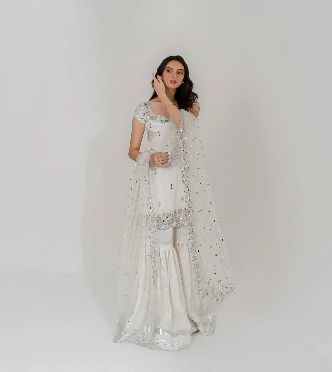 Woman wearing a white saree with silver embroidery on a plain background
