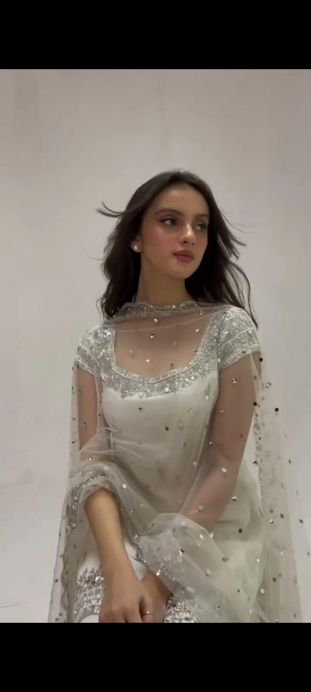 Woman wearing a white embroidered dress with a plain background