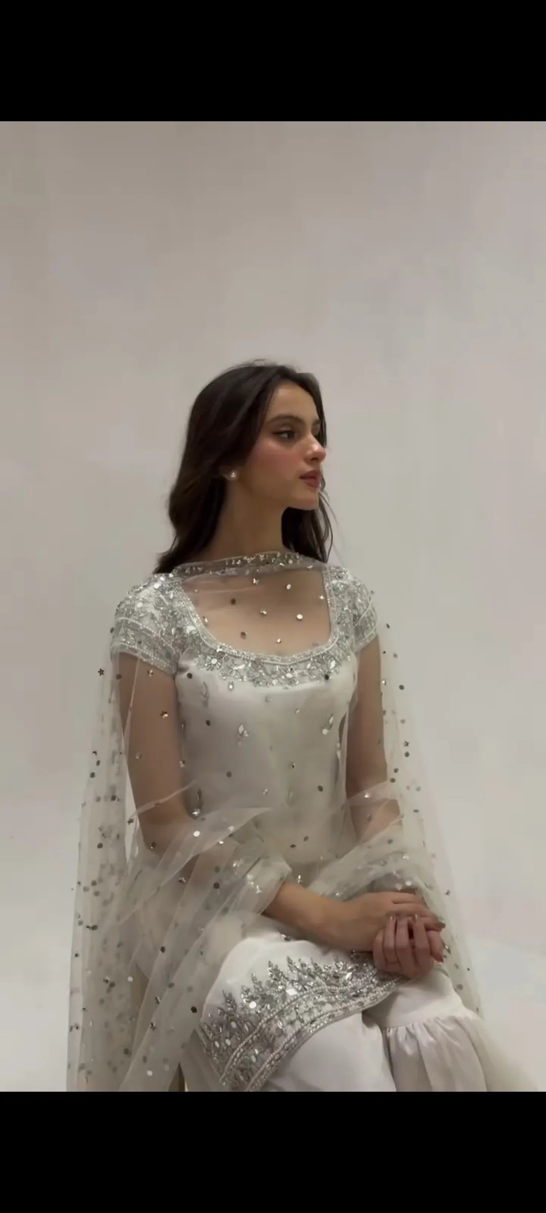 Woman wearing a white embroidered saree with a plain background