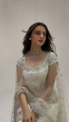 Woman wearing a white embroidered dress with a plain background