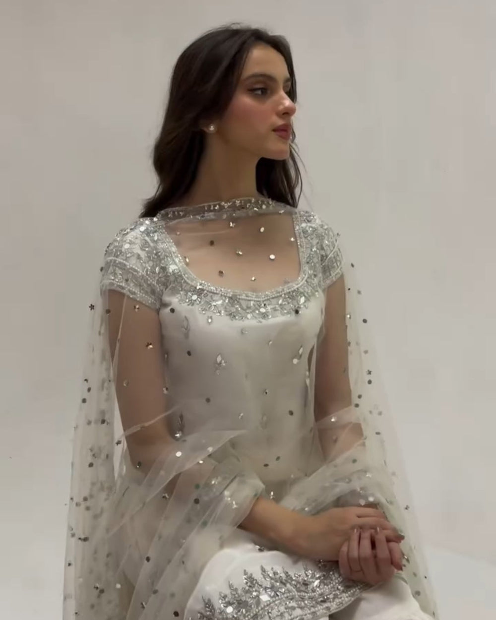 Woman wearing a white traditional outfit with intricate detailing on a plain background