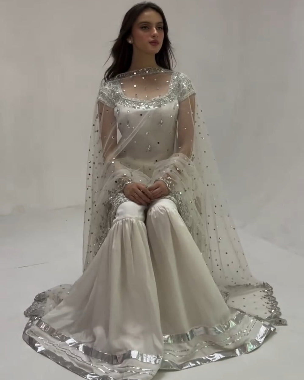 Woman wearing a white embroidered traditional outfit on a plain background