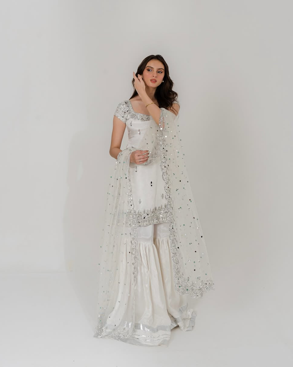 Woman wearing a white traditional outfit with a sheer dupatta against a plain background