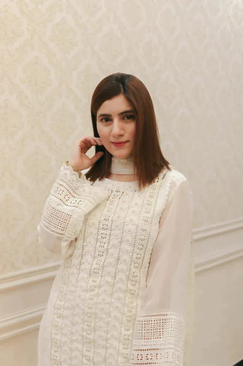 Woman wearing a white lace outfit against a light-colored wall.