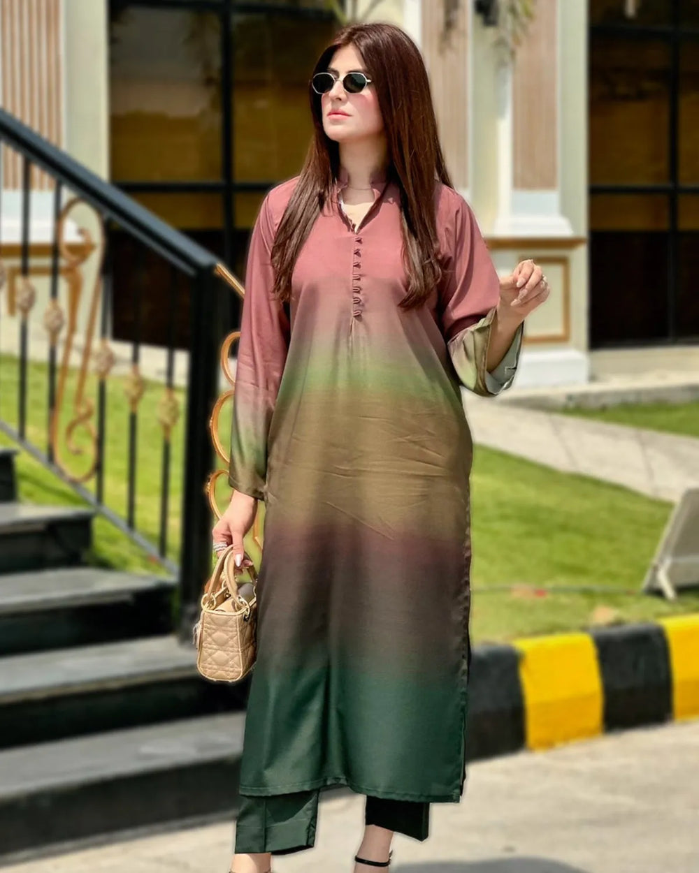 Woman wearing a gradient dress standing outdoors with greenery and steps in the background