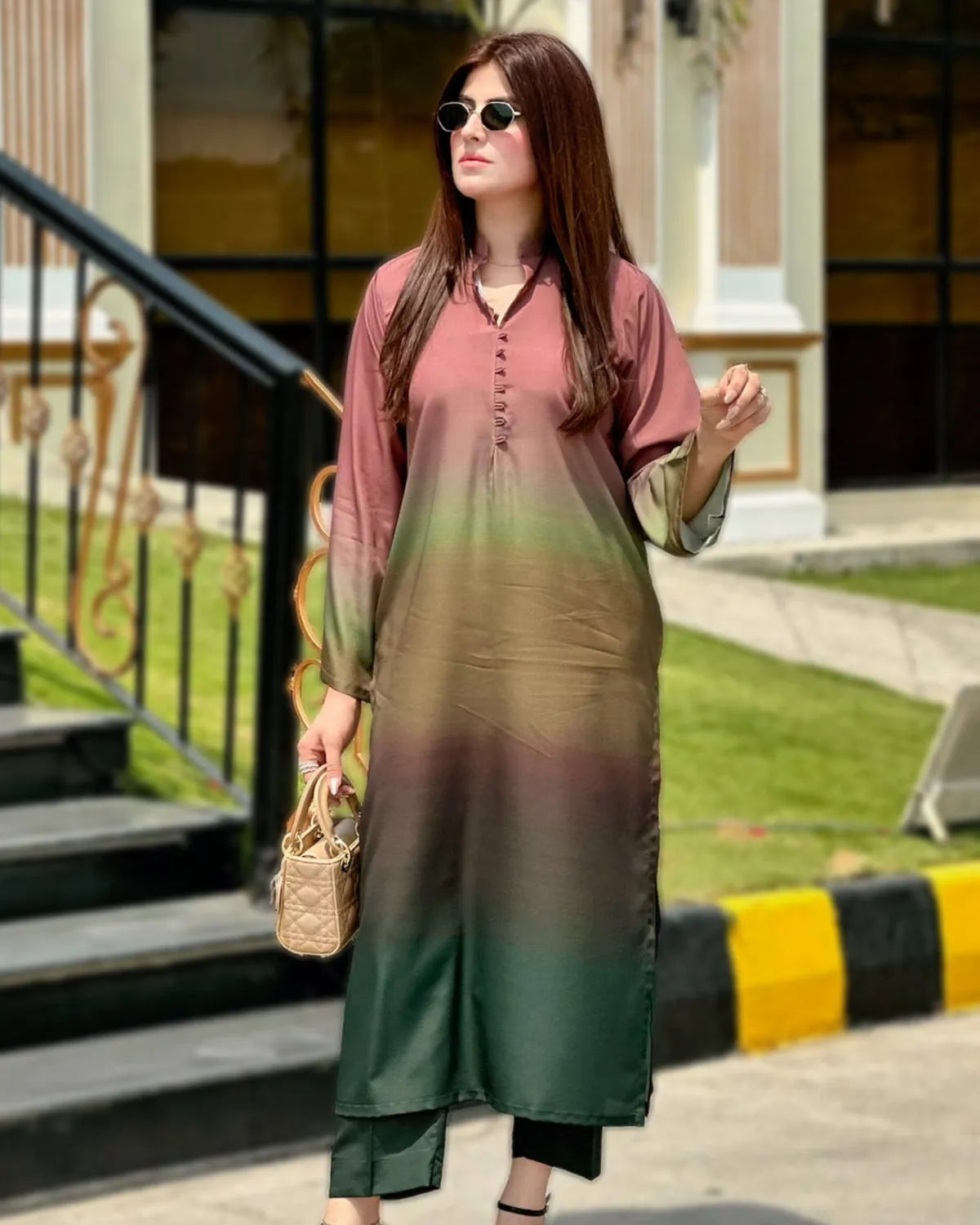 Woman wearing a gradient dress standing outdoors with greenery and steps in the background