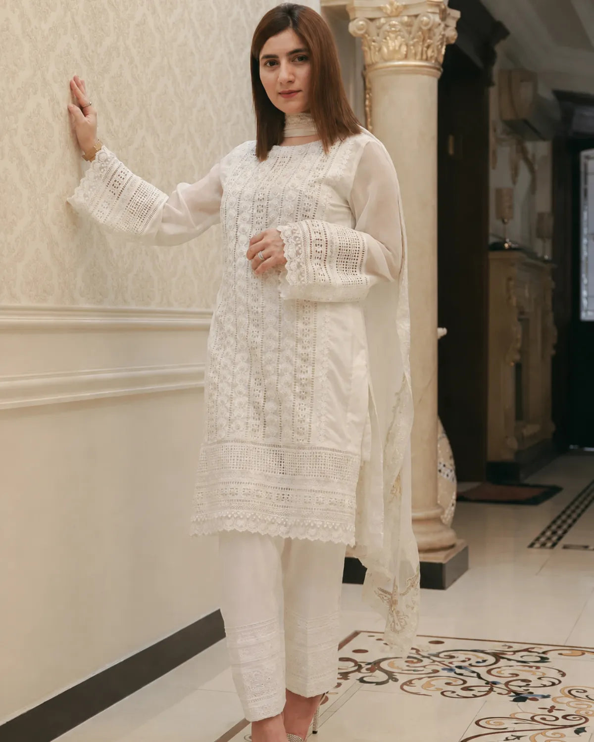Woman in a white traditional outfit standing indoors with decorative columns and floor.