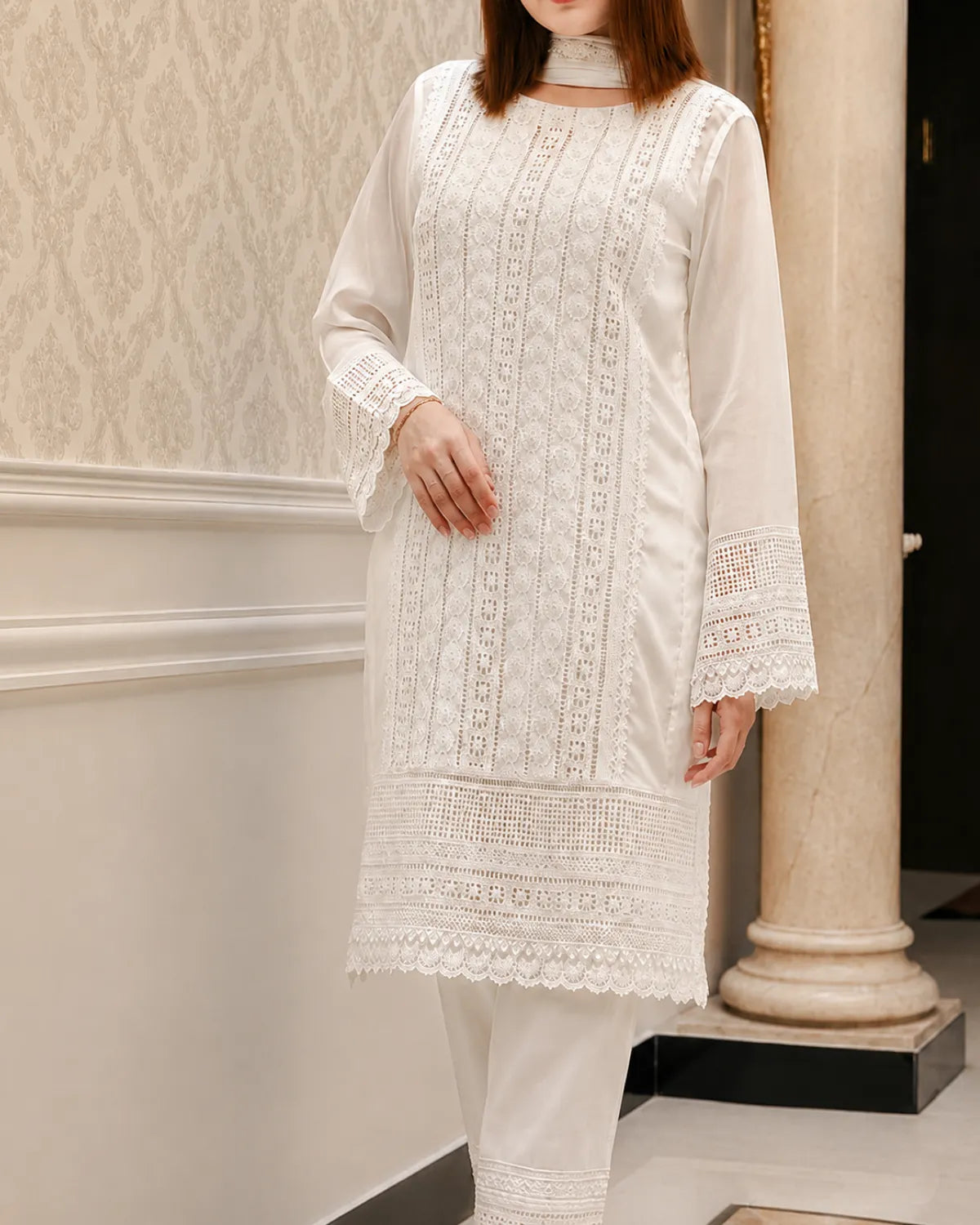 Person wearing a white embroidered outfit standing against a neutral wall.