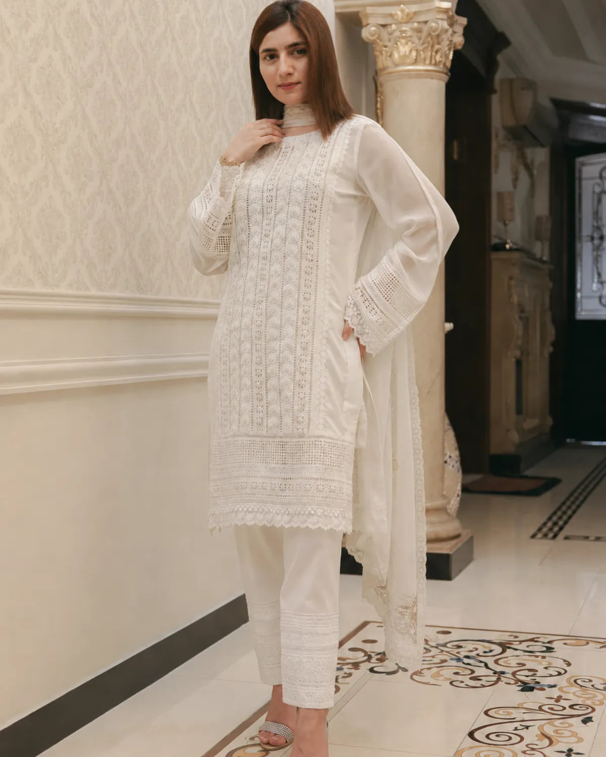 Woman wearing a white embroidered outfit in an elegant interior setting
