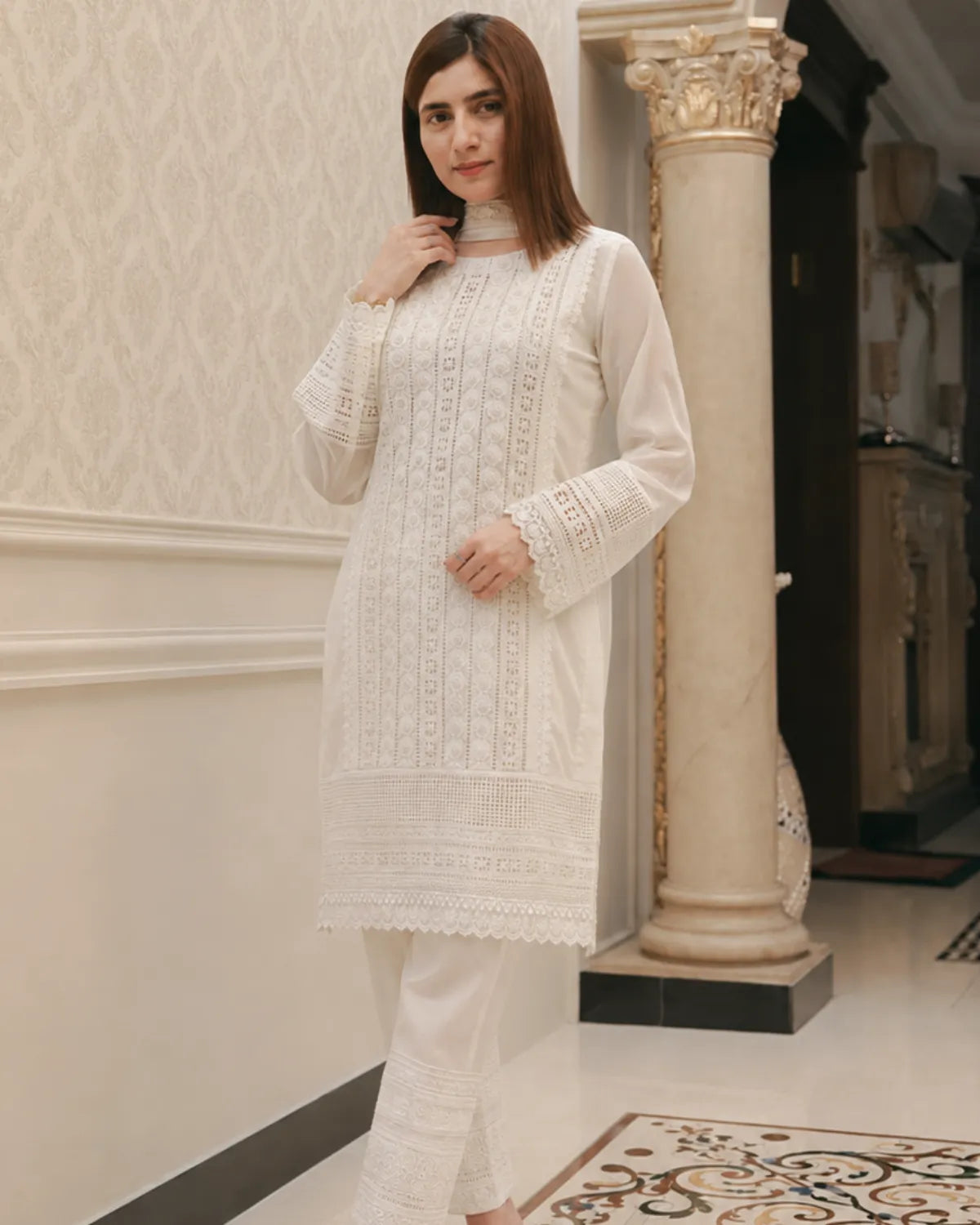 Woman wearing a white embroidered outfit in an elegant interior setting